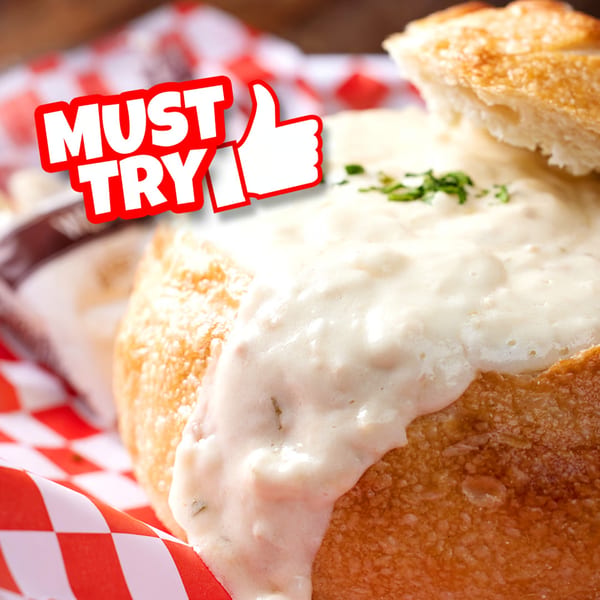 Creamy clam chowder in a bread bowl with a "MUST TRY" label and a thumbs-up icon.