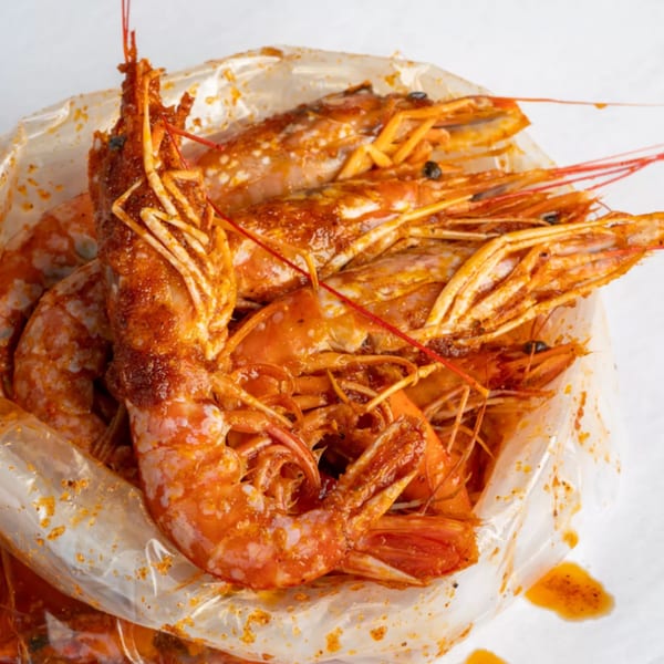 A plastic bag filled with Crab N' Spice's seasoned, shell-on shrimp, glistening with sauce.