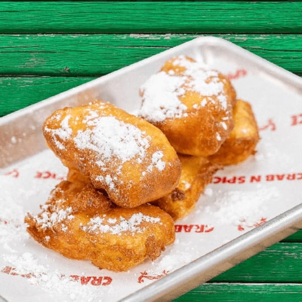 Golden brown hushpuppies dusted with powdered sugar on a metal tray with Crab N' Spice branded paper.