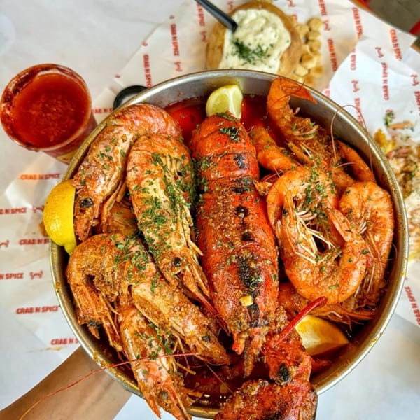 A large metal bowl of Crab N' Spice seafood boil with lobster, shrimp, and lemon.