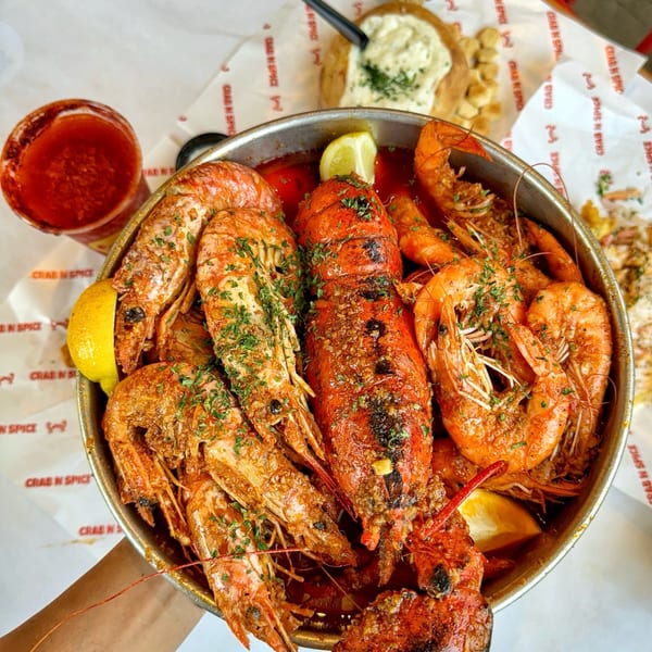 A large metal bowl of Crab N' Spice seafood boil with lobster, shrimp, and lemon wedges.